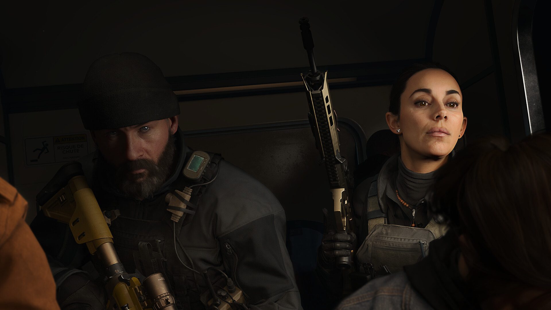 Two armed Operators sit inside a dimly lit transport vehicle, carrying tactical equipment and weapons while preparing for a mission during transit.