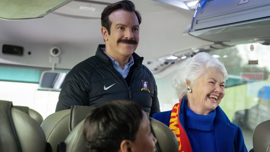 Ted e Mae sorrindo dentro de um ônibus em Ted Lasso